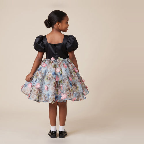 Back view of a black satin girls party dress with puff sleeves, square back and floral 3D flower skirt.