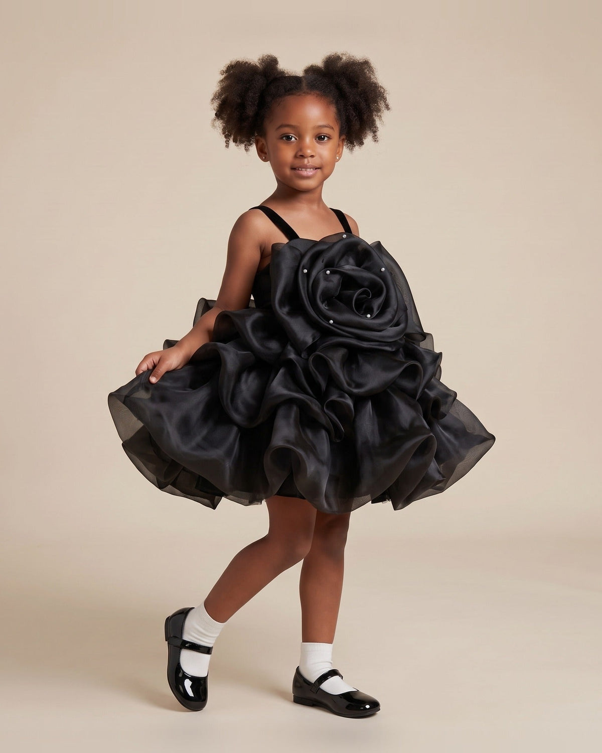 Girl wearing a black organza girls party dress with an oversized rosette bodice, velvet straps and a ruffled tutu skirt.