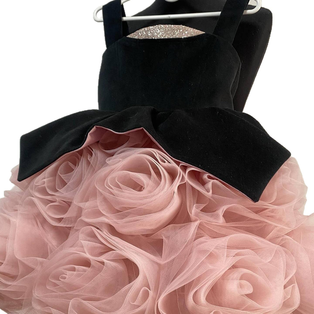 Black velvet peplum flaring over the blush rosette skirt on this girls party dress, angled side view.