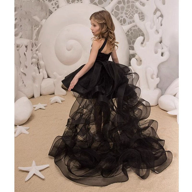 Black dress for girls showing the ruffled organza train sweeping behind, back view.