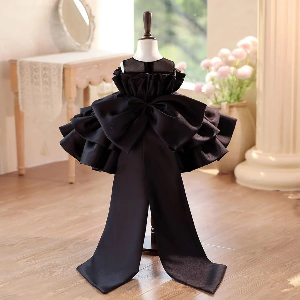 Back view of the black dress for girls showing the large satin bow and the two long train panels.
