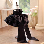 Black satin girls formal dress with the back bow and train spread out, angled back view.