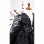 Close-up of the sequin bodice, pearl buttoned bow and sheer sequin sleeve on the black gown.