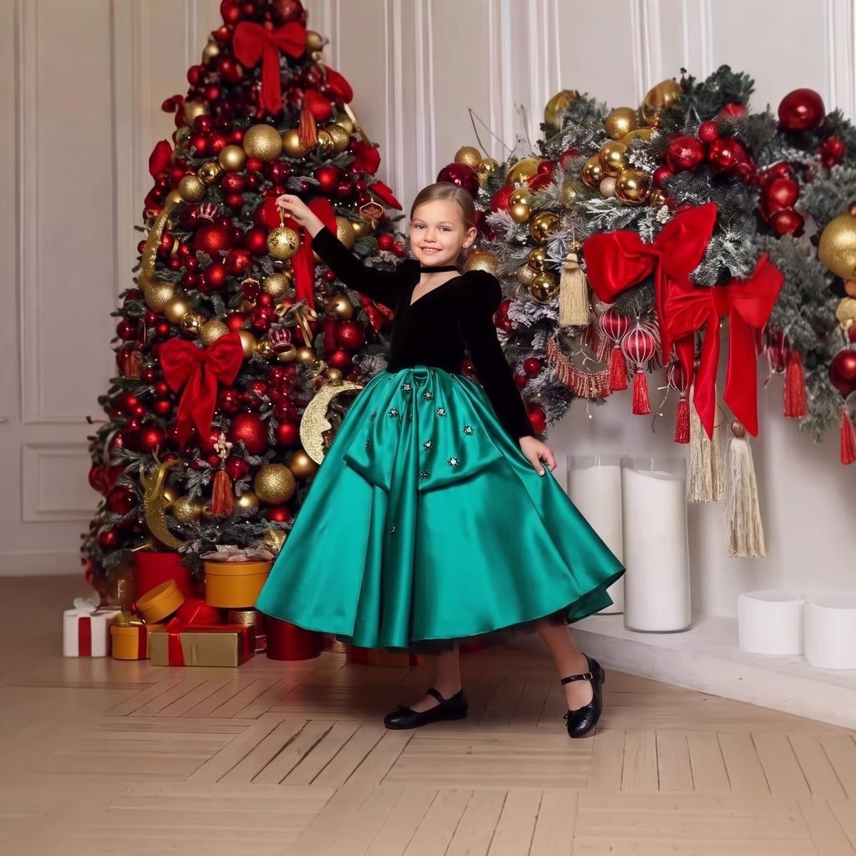 Girl hanging an ornament on a Christmas tree in a black velvet and emerald green satin holiday dress with puff sleeves and jeweled bow