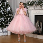 Pink feather cape flower girl dress worn beside a decorated tree, showing the gathered ruffled hem of the tulle skirt.
