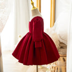 Burgundy satin girls party dress with a gathered full skirt and puff sleeve, side view, one of our girls formal dresses.