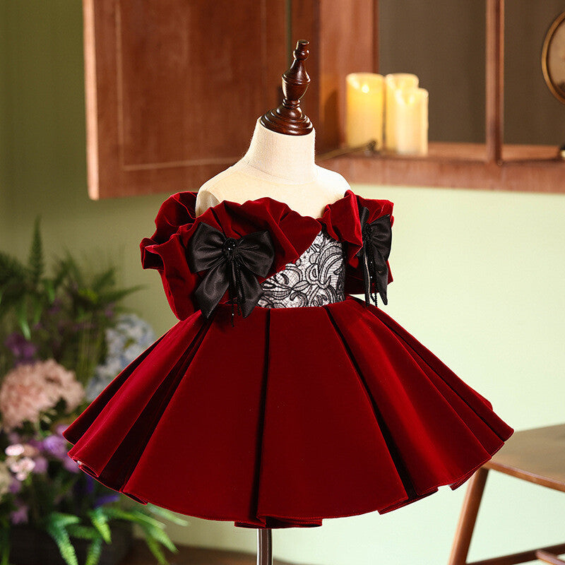 Angled front view of the burgundy velvet girls party dress, showing the pleated velvet skirt and black satin bows, one of our girls holiday dresses.