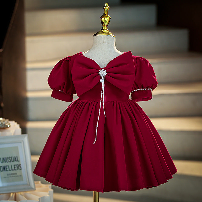 Burgundy velvet girls dress back view with a large bow, pearl brooch and puff sleeves, designed for Christmas and holiday parties.