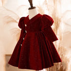 Burgundy glitter velvet princess dress for girls seen from the side, showing the puff sleeves and the gathered skirt.