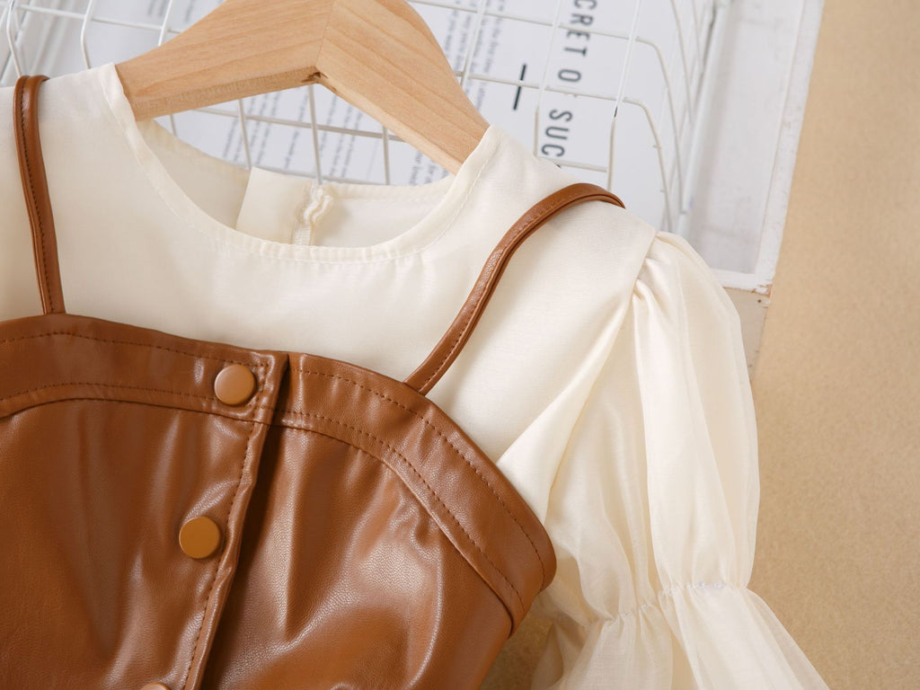 Close-up of the brown faux leather vest with thin straps and snap buttons over the cream chiffon girls dress, designed for parties.