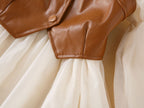 Pointed hem of the brown faux leather vest over the gathered cream chiffon skirt of the girls dress, designed for parties.