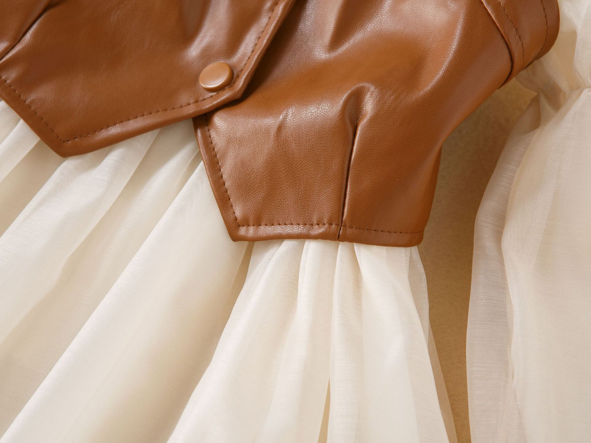 Pointed hem of the brown faux leather vest over the gathered cream chiffon skirt of the girls dress, designed for parties.