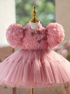Round puff sleeves covered in fabric rosettes on this dusty rose girls party dress, angled side view.