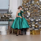 Emerald green satin girls dress with one-shoulder neckline and full tea-length skirt, designed for holiday photos.