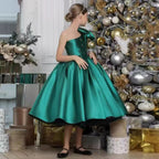 Emerald green satin girls dress with one-shoulder bow and beaded flowers, designed for Christmas parties.
