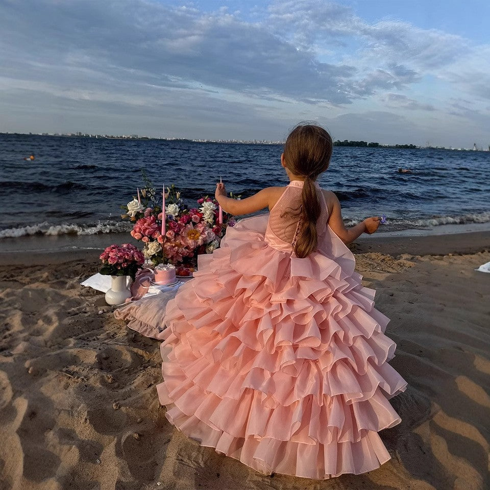 Girl standing on the beach in the blush pink tiered organza gown, back view, for a beach wedding.