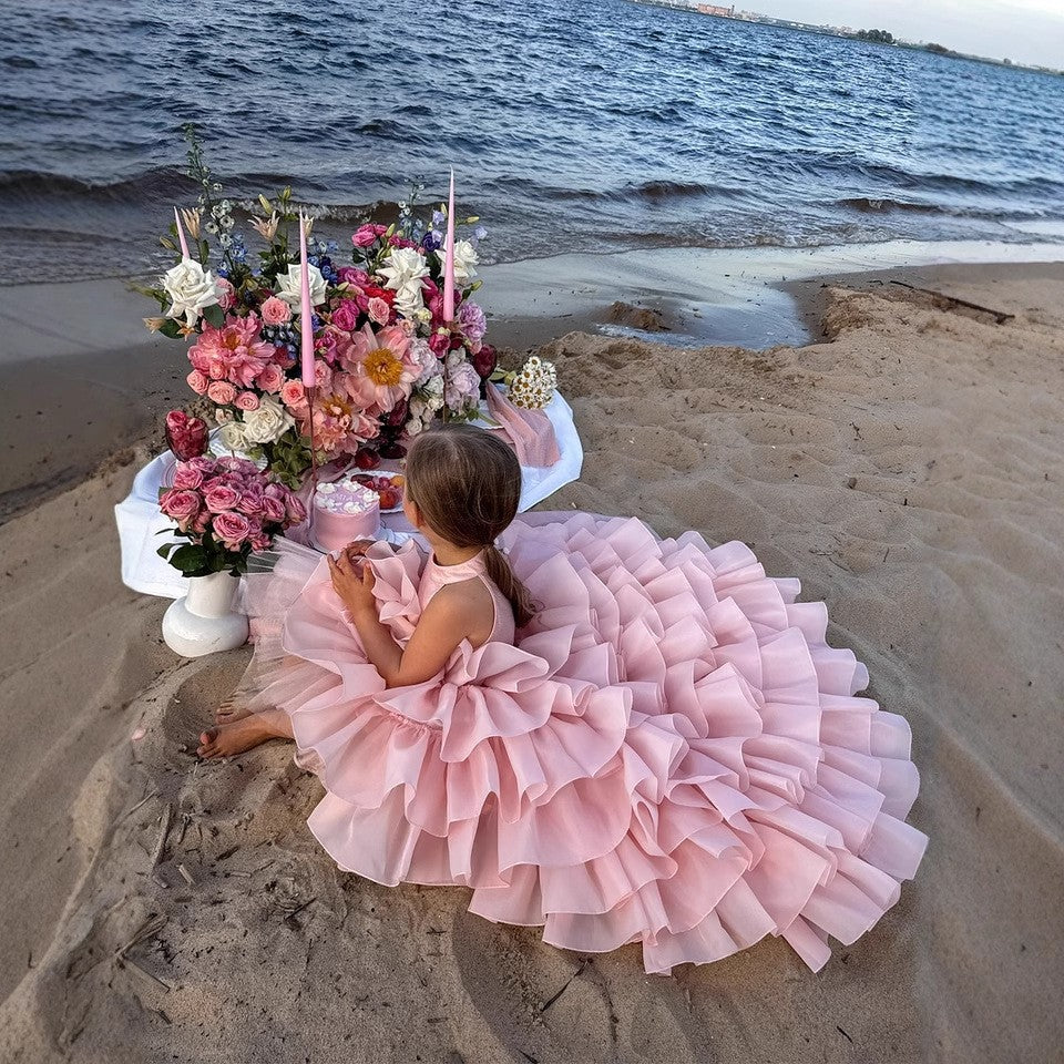 Girl seated on the sand in the blush pink organza ball gown with the ruffled skirt fanned out around her.