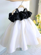 Ivory and black satin girls party dress with an off-shoulder black ruffle bodice and straps, designed for first birthdays.