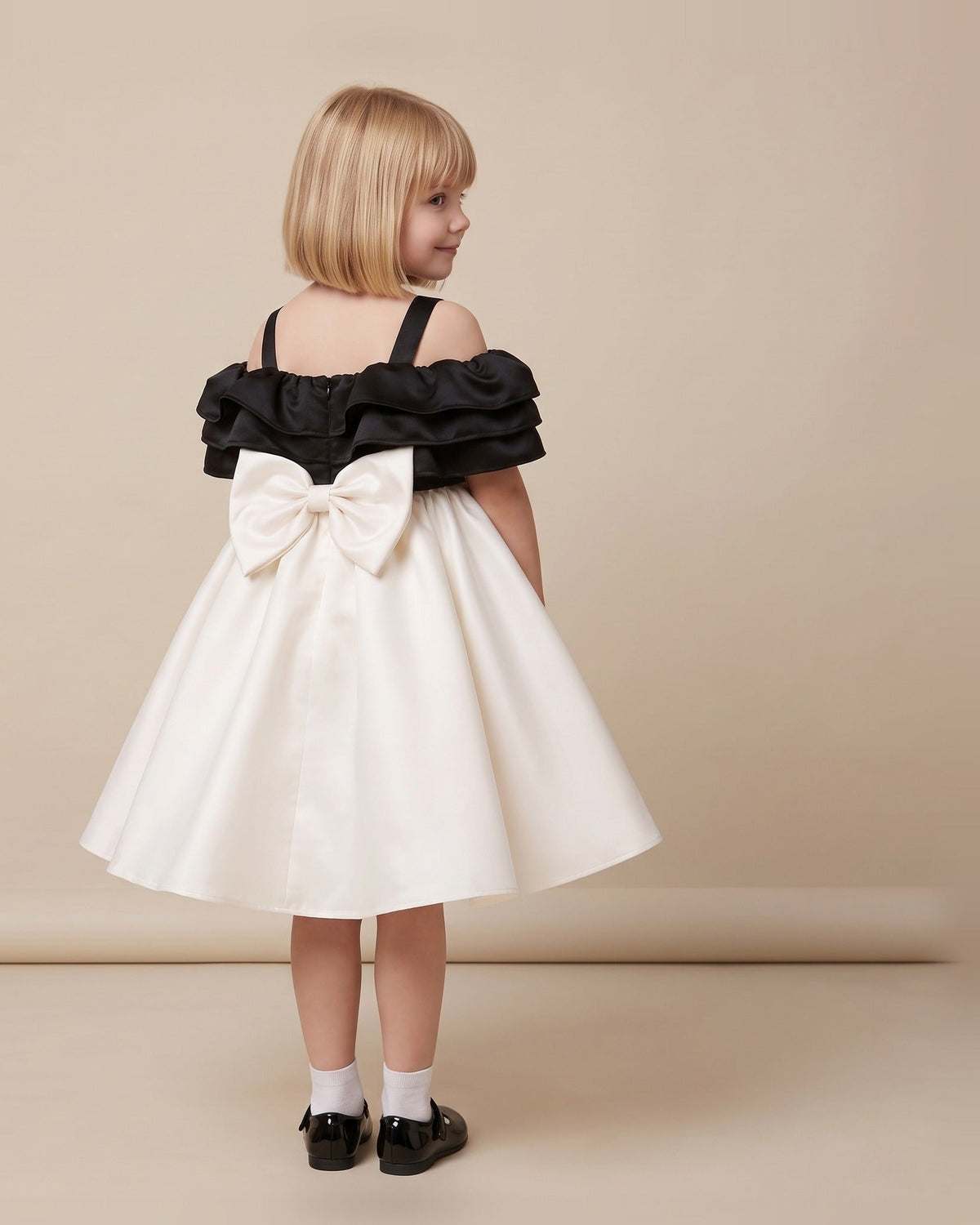 Back view of an ivory and black satin girls party dress with a large ivory bow at the back of the waist.