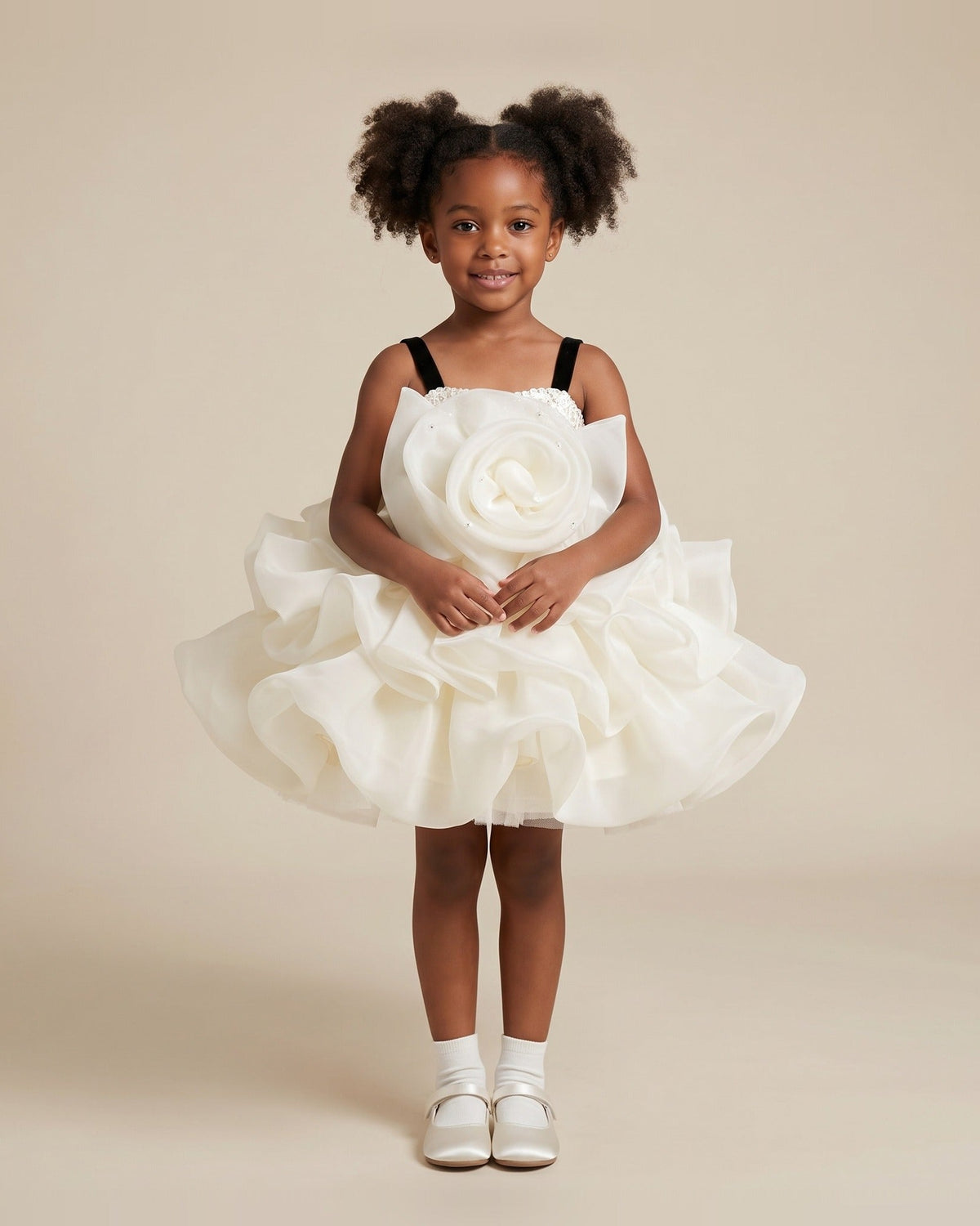 Girl wearing an ivory organza girls party dress with an oversized rosette bodice, black velvet straps and a ruffled tutu skirt, front view.