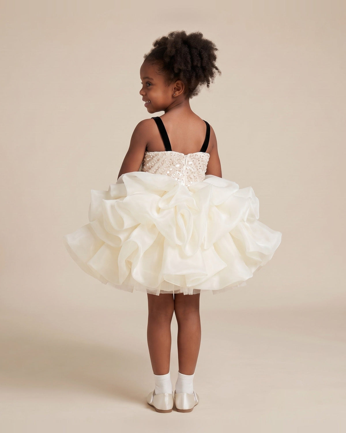 Back view of an ivory organza girls party dress with a sequin back bodice and black velvet straps.