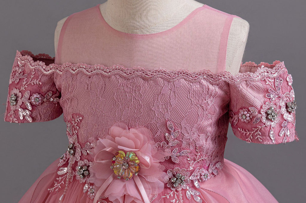 Pink lace girls gown close-up of beaded off-shoulder sleeves and illusion neckline, designed for formal events.