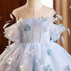 Close-up of the pearl-trimmed off-shoulder bodice, 3D flowers and feather accents on the light blue girls formal dress.