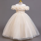 Champagne tulle girls ball gown with off-shoulder ruffle neckline, beaded lace waist and back bow, designed for weddings and flower girls.
