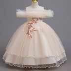 Champagne tulle girls ball gown with ruffled off-shoulder neckline, floral appliqué and satin bow back, designed for weddings and parties.