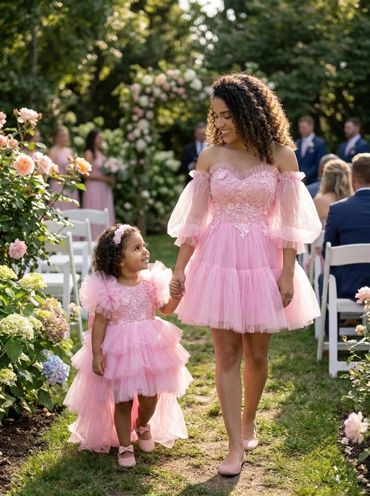 Mother and daughter walking through a garden wedding in matching pink tiered tulle dresses