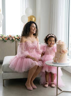 Mother and daughter seated beside a pink birthday cake in matching pink tulle dresses