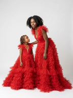 Angled studio view of the matching red tulle mommy and daughter gowns showing the tiered ruffle skirts and trains