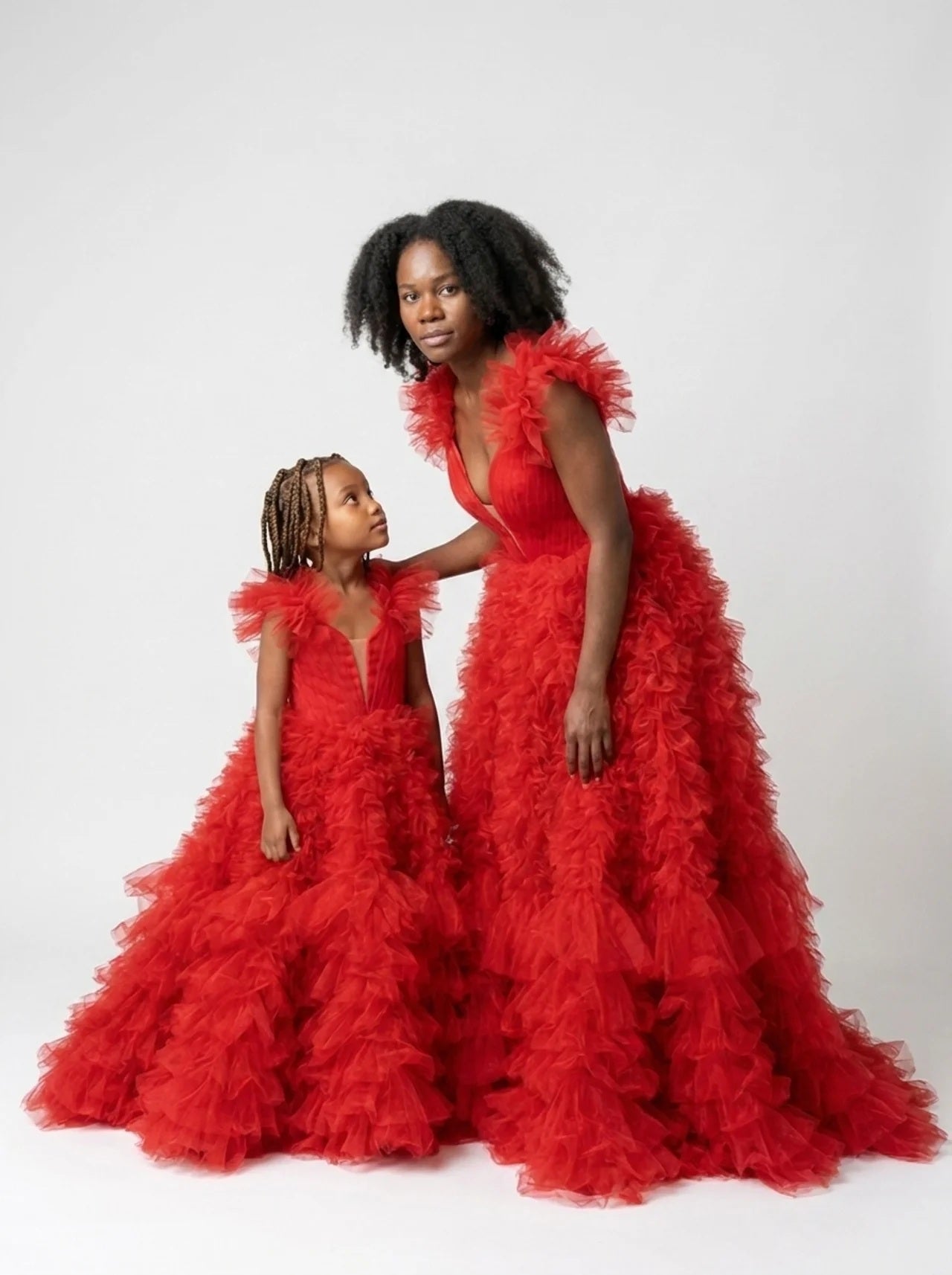 Angled studio view of the matching red tulle mommy and daughter gowns showing the tiered ruffle skirts and trains