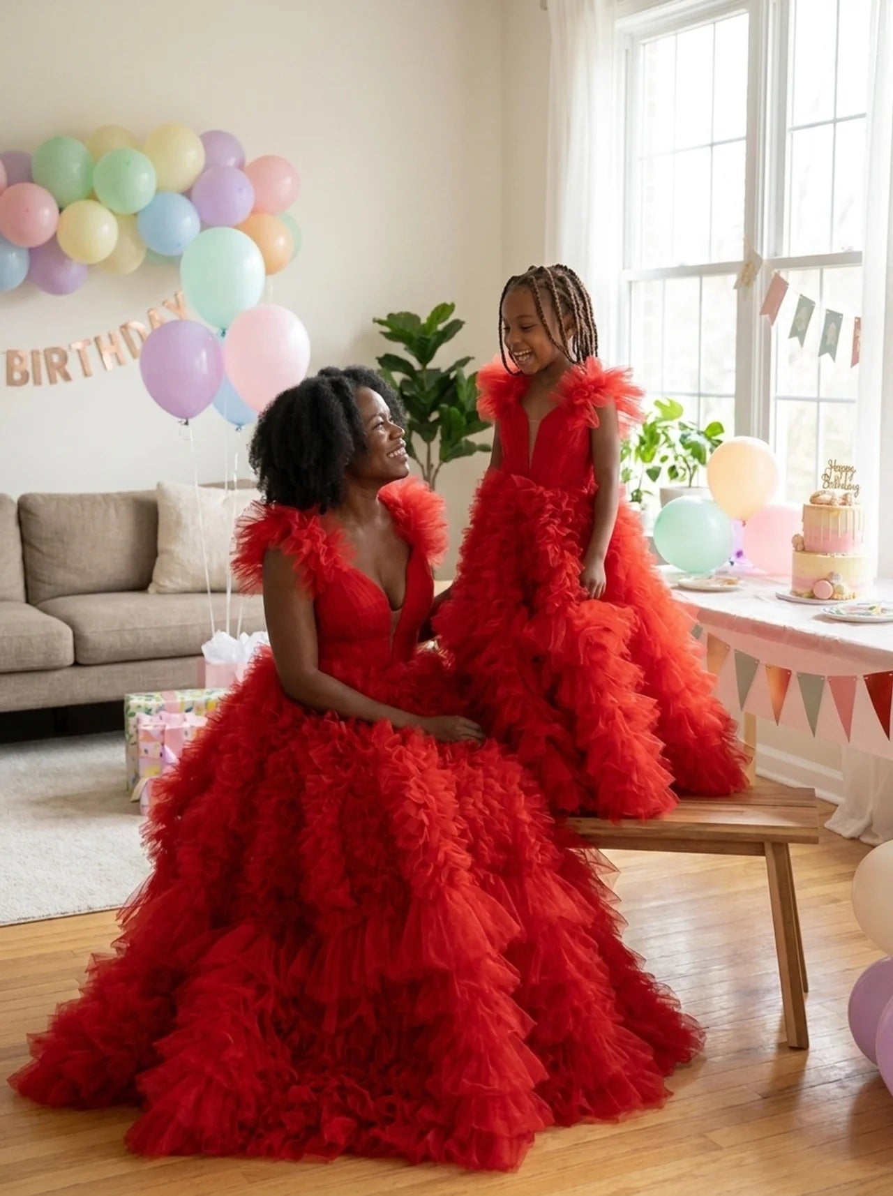 Mother and daughter in matching red tulle ball gowns at a birthday party with balloons and cake