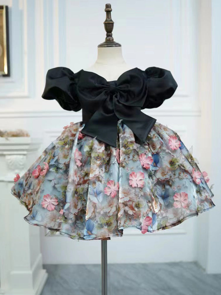 Black satin girls party dress with an oversized front bow, puff sleeves and a 3D floral skirt, designed for birthday parties.