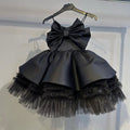 Black satin girls party dress with an oversized front bow and tiered tulle skirt, front view, for birthday parties.
