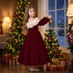 Girl in a red velvet Christmas dress hanging an ornament on the Christmas tree on Christmas Eve