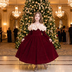 Girl curtsying in a red sparkle velvet gown in front of a giant Christmas tree at a holiday gala