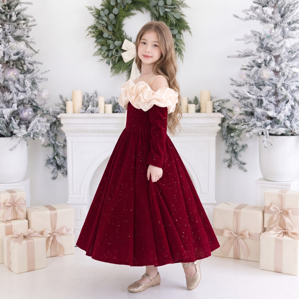 Side view of a girls red velvet ball gown with puffy ivory ruffles over the shoulders and a full sparkle skirt