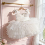 White tulle flower girl dress hanging on a gold rail against a pink wall, view 2.