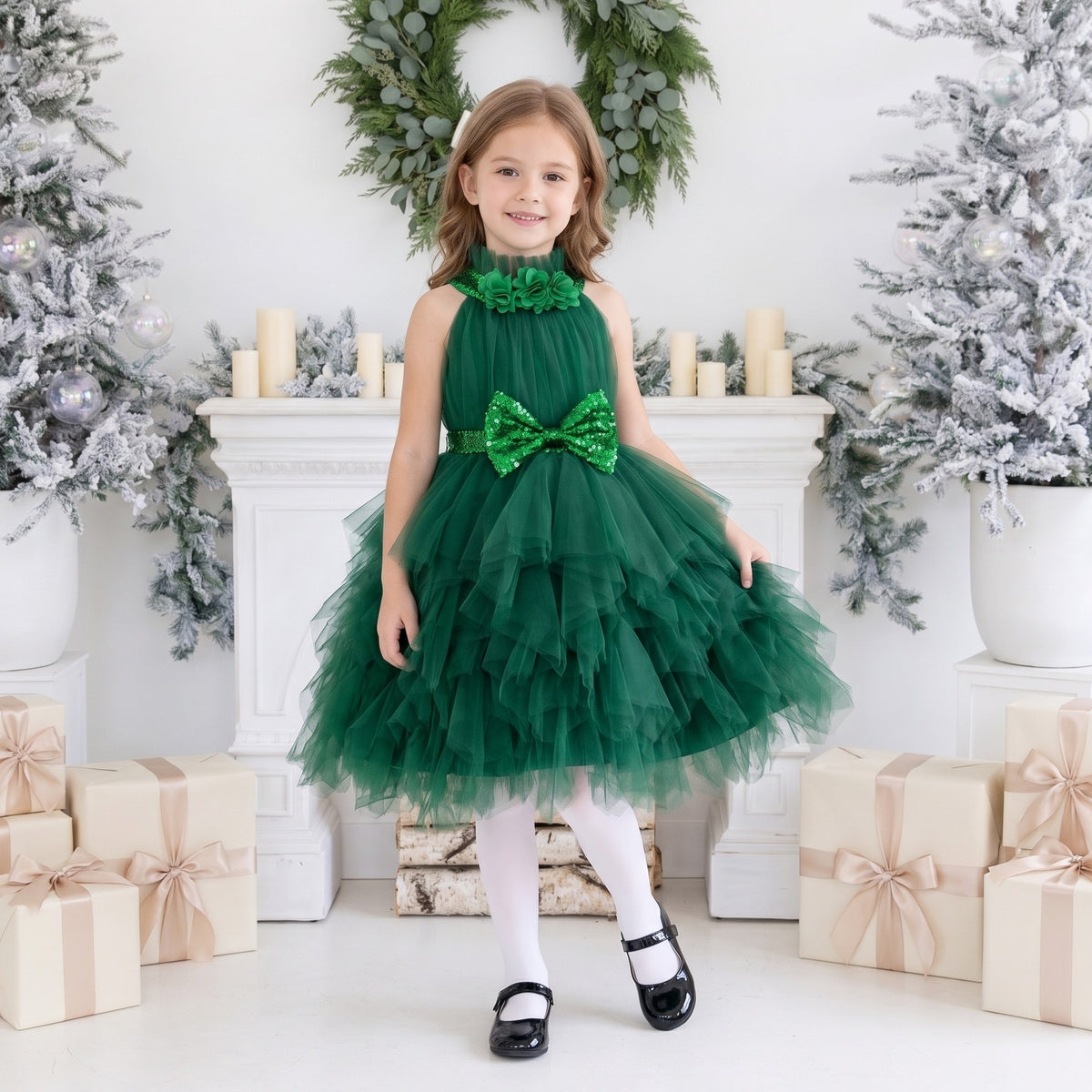 Dark green tiered tulle girls Christmas dress with a ruffled high collar, fabric flowers and a sequin bow, worn in a Christmas studio.