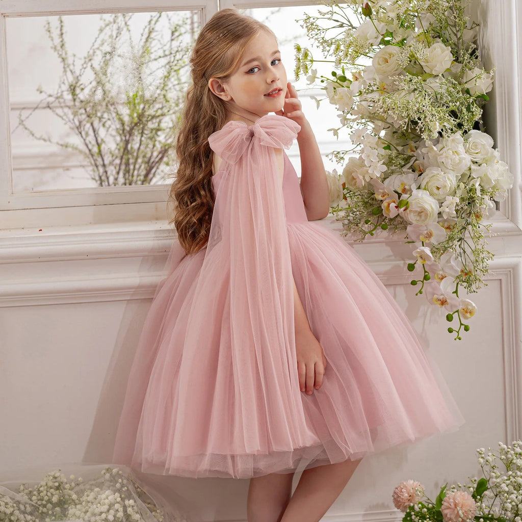 Blush pink tulle girls party dress photographed beside white flowers, angled view, for a photo session.
