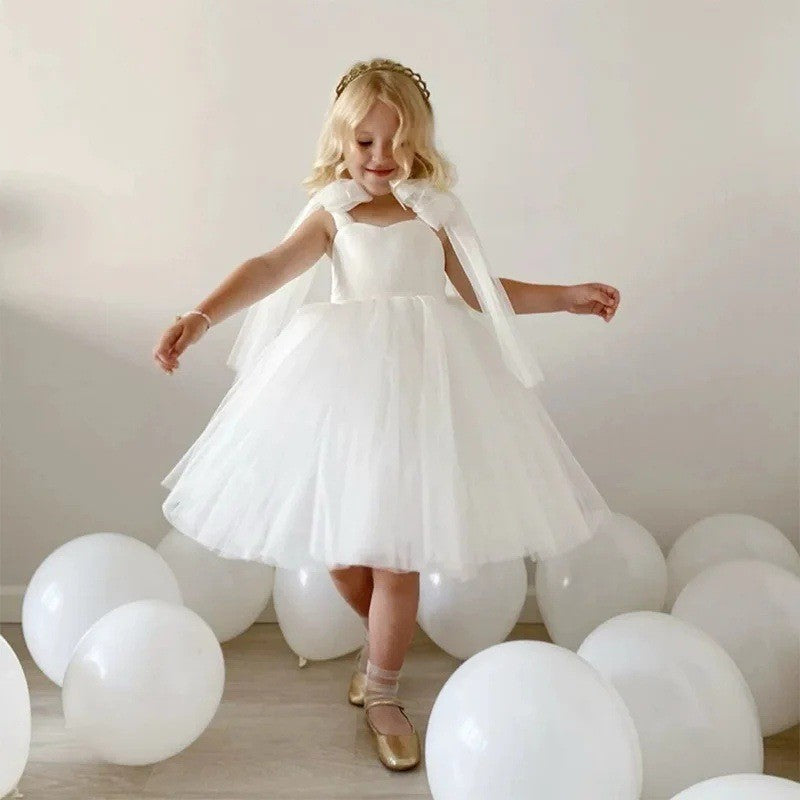 White tulle flower girl dress with an oversized shoulder bow, front view, for a wedding ceremony.