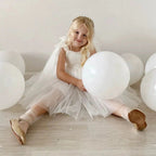 Girl sitting in the white tulle girls party dress with the skirt spread around her, for a birthday celebration.